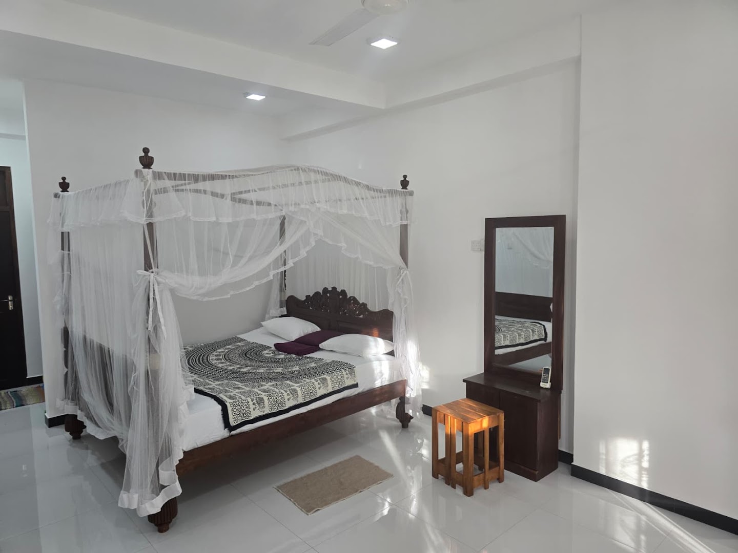 A bright bedroom with a carved timber bed and white mosquito net