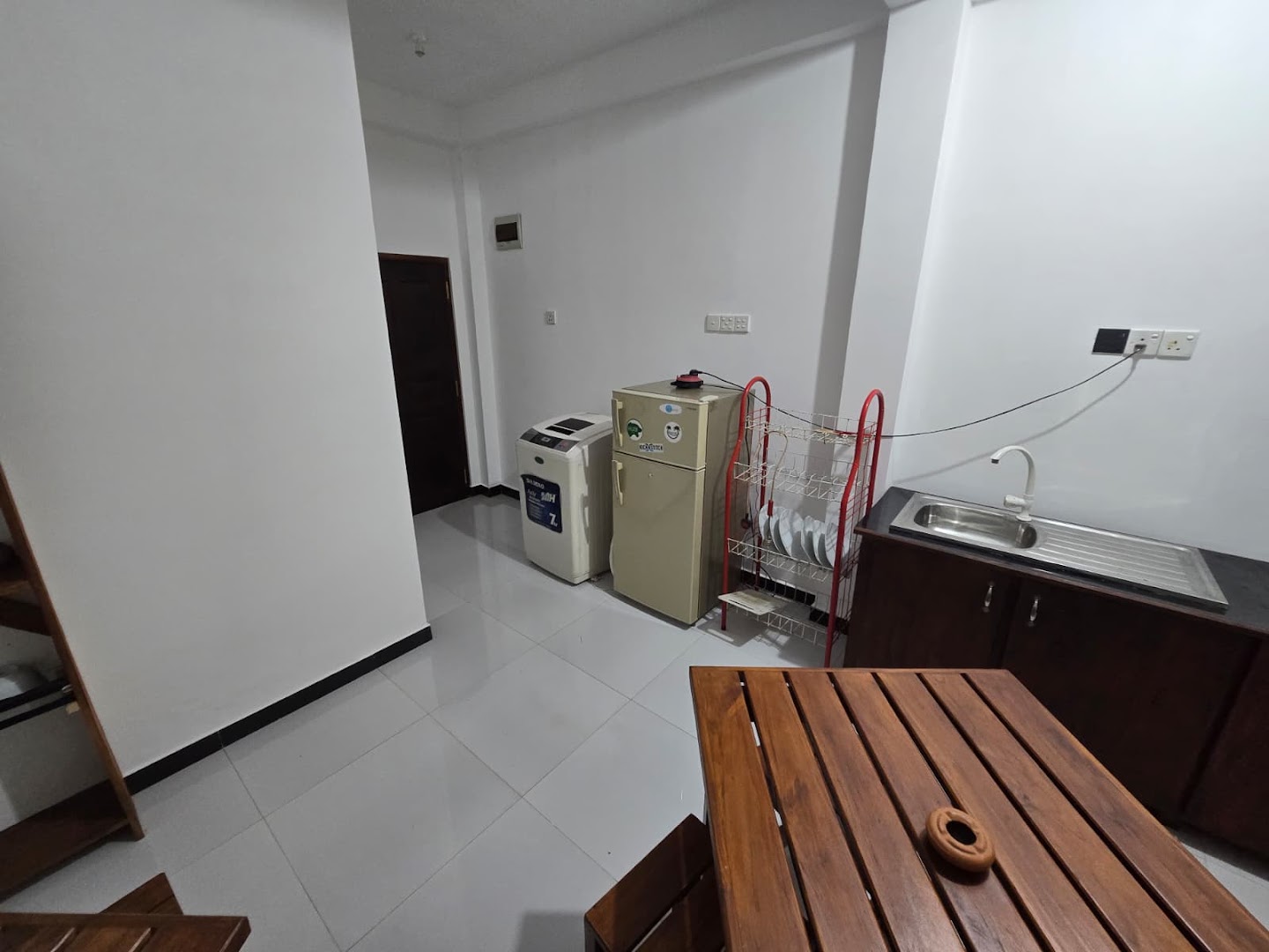 A bright interior with a sink, refrigerator, drying rack, and timber table